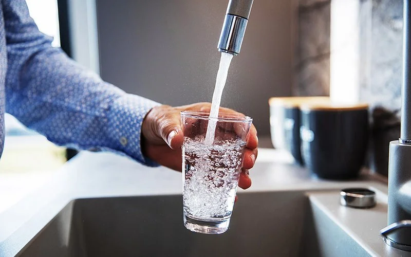 Ein Mann hält ein Glas unter den Wasserhahn und befüllt es mit Trinkwasser.