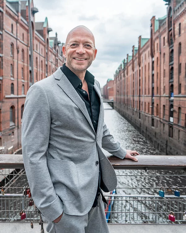 Eric Hegmann auf einer Brücke in der Hamburger Speicherstadt, die linke Hand am Geländer, die rechte Hand in der Hosentasche.