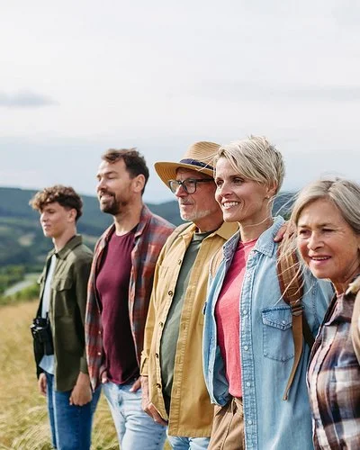 Fünf Menschen verschiedener Generationen stehen gemeinsam auf einer Wiese und blicken in die Landschaft.