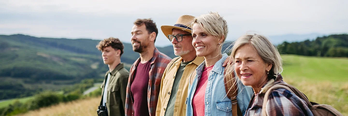 Fünf Menschen verschiedener Generationen stehen gemeinsam auf einer Wiese und blicken in die Landschaft.