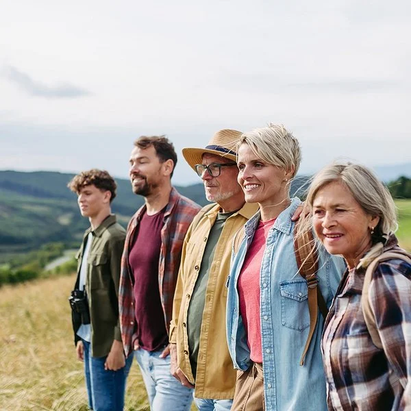 Fünf Menschen verschiedener Generationen stehen gemeinsam auf einer Wiese und blicken in die Landschaft.