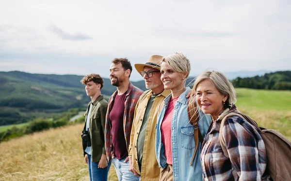 Fünf Menschen verschiedener Generationen stehen gemeinsam auf einer Wiese und blicken in die Landschaft.