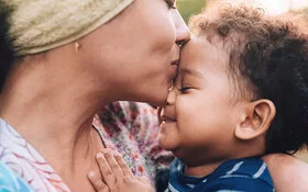 Mutter hält ihr Baby liebevoll im Arm und küsst es, da Zuneigung für die Entwicklung eines Babys essenziell ist.