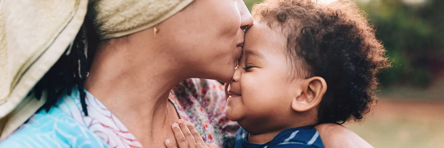 Mutter hält ihr Baby liebevoll im Arm und küsst es, da Zuneigung für die Entwicklung eines Babys essenziell ist.