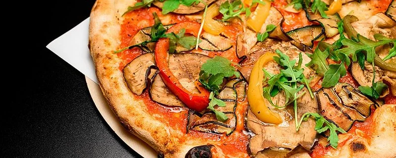 Nahaufnahme einer Gemüsepizza, serviert auf einem Holzbrett.