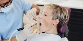 Ein Zahnarzt behandelt eine Patientin mit dem Bohrer. Ist der Zahn nicht mehr zu retten, benötigt sie Zahnersatz. 