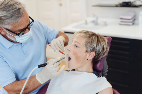 Ein Zahnarzt behandelt eine Patientin mit dem Bohrer. Ist der Zahn nicht mehr zu retten, benötigt sie Zahnersatz. 