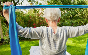 Eine ältere Frau trainiert mit einem Fitnessband im Sitzen.