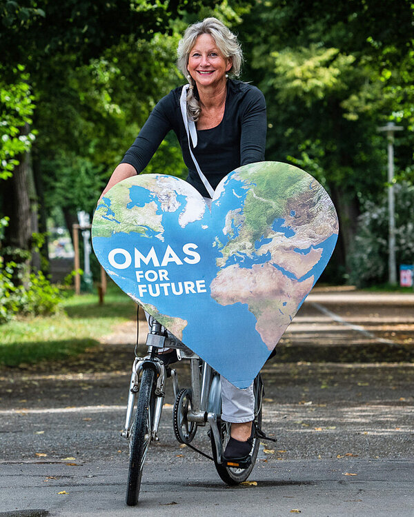 Cordula Weimann auf einem Fahrrad und einem herzförmigen Pappschild mit der Aufschrift “Omas for Future”