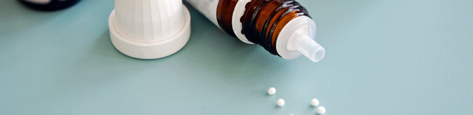 Vor einer Flasche eines homöopathischen Arzneimittels liegen Globuli-Kügelchen.