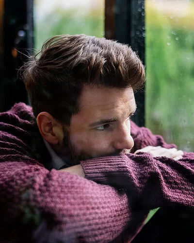Männer-Gesundheit und Depression: Ein nachdenklicher Mann schaut bei Regen aus dem Fenster.