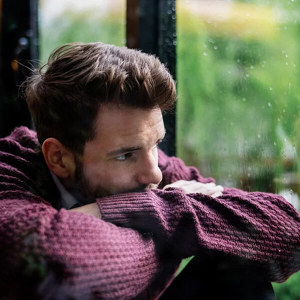 Männer-Gesundheit und Depression: Ein nachdenklicher Mann schaut bei Regen aus dem Fenster.