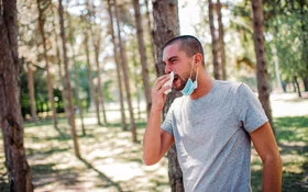 Ein Mann mit Heuschnupfen putzt sich im Wald die Nase.