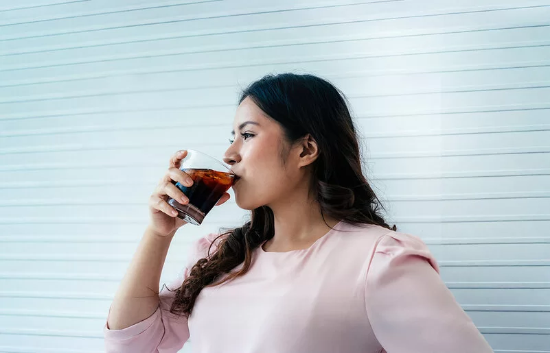 Eine Frau trinkt aus einem Glas ein Erfrischungsgetränk.