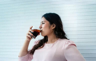 Eine Frau trinkt aus einem Glas ein Erfrischungsgetränk.