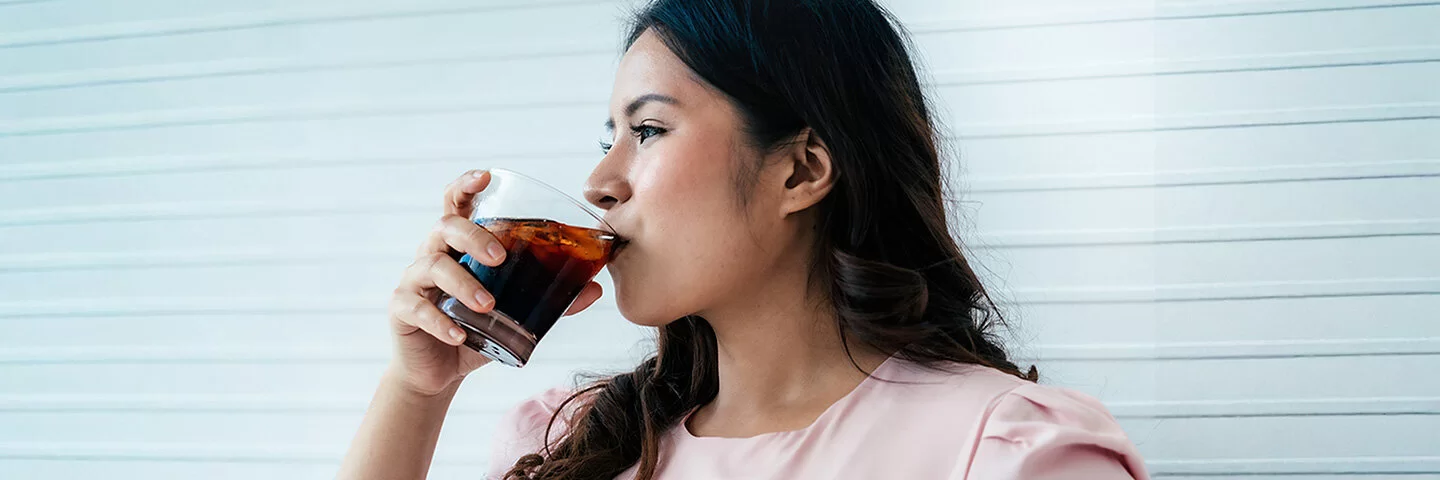 Eine Frau trinkt aus einem Glas ein Erfrischungsgetränk.