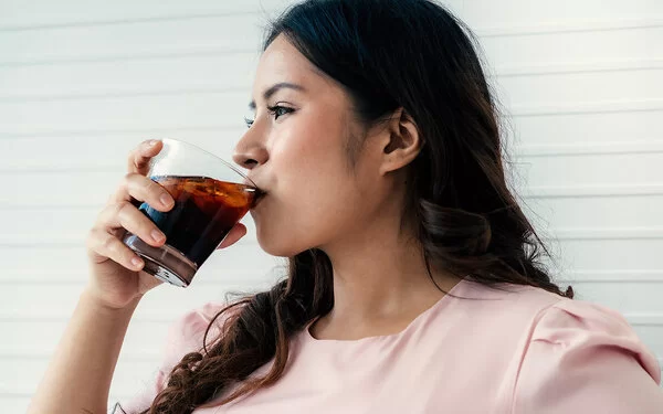 Eine Frau trinkt aus einem Glas ein Erfrischungsgetränk.