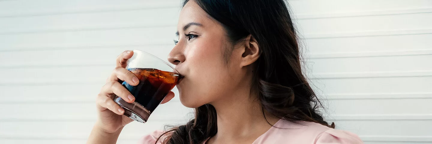 Eine Frau trinkt aus einem Glas ein Erfrischungsgetränk.