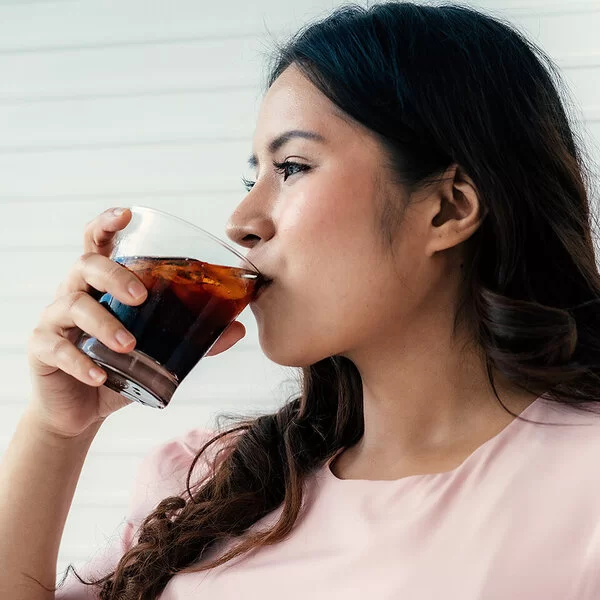 Eine Frau trinkt aus einem Glas ein Erfrischungsgetränk.