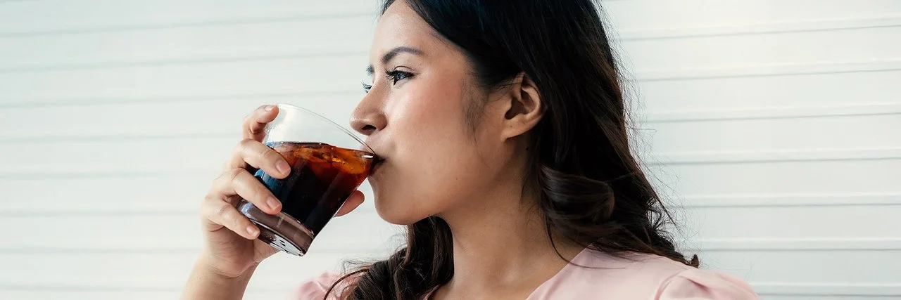 Eine Frau trinkt aus einem Glas ein Erfrischungsgetränk.