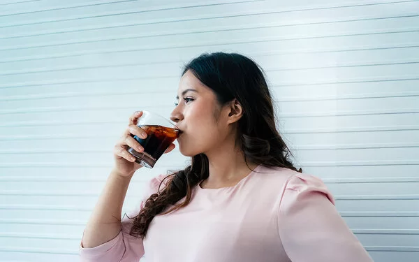 Eine Frau trinkt aus einem Glas ein Erfrischungsgetränk.