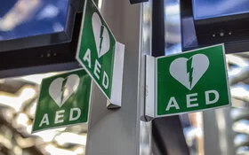 Grüne Hinweisschilder an einem Pfosten, die den Standort eines Defibrillators kennzeichnen.
