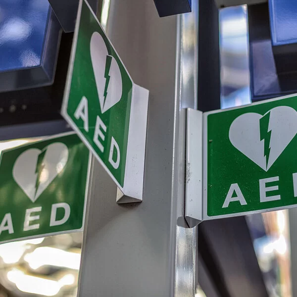 Grüne Hinweisschilder an einem Pfosten, die den Standort eines Defibrillators kennzeichnen.