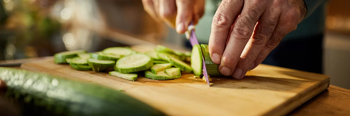 Auf einem Holzbrett wird eine rohe Zucchini in Scheiben geschnitten.