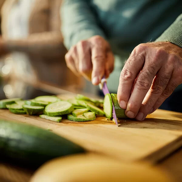 Auf einem Holzbrett wird eine rohe Zucchini in Scheiben geschnitten.