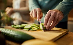 Auf einem Holzbrett wird eine rohe Zucchini in Scheiben geschnitten.