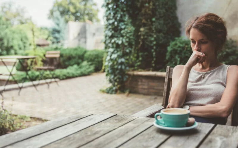 Depressive Frau sitzt am Tisch mit Kaffeebecher