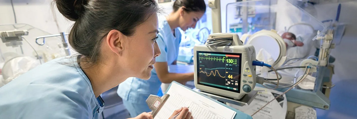 Intensivpflege: Zwei Pflegefachpersonen versorgen ein Baby, das in einem Brutkasten liegt.