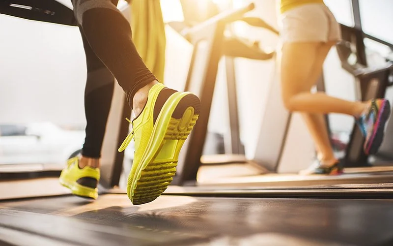 Zwei Personen trainieren auf dem Laufband im Fitnessstudio.