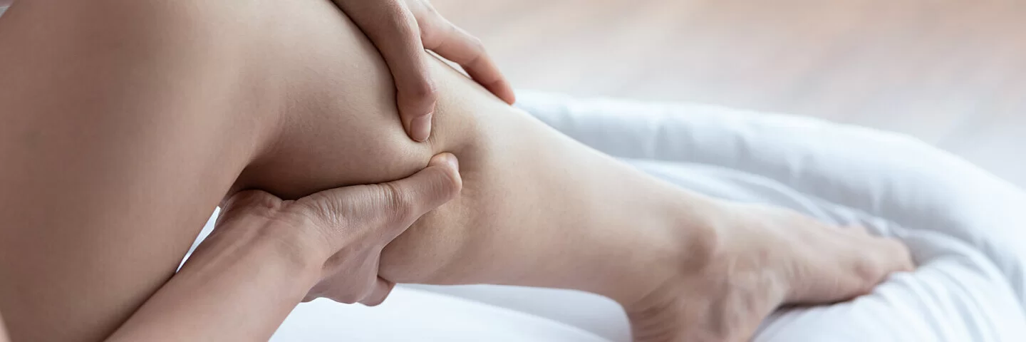 Eine Frau sitzt auf dem Bett und hält ihre unruhigen Beine.
