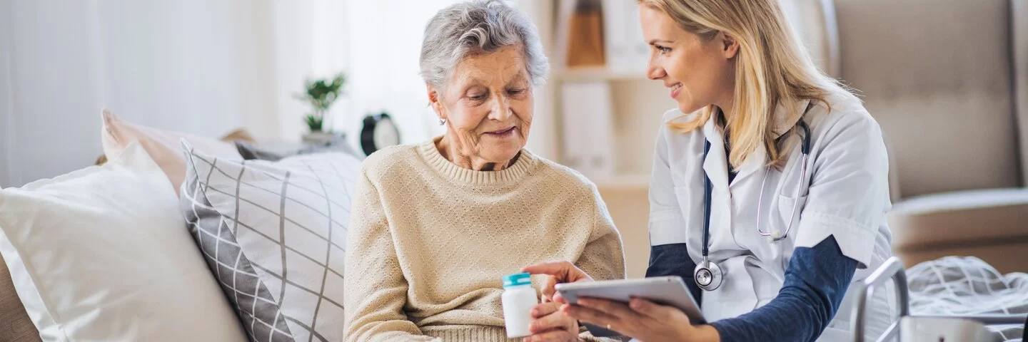 Praxisassistentin erklärt älterer Dame eine Medikation und hält ein Tablet in der Hand.