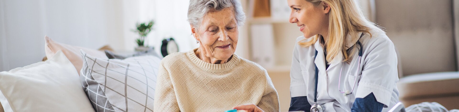 Praxisassistentin erklärt älterer Dame eine Medikation und hält ein Tablet in der Hand.