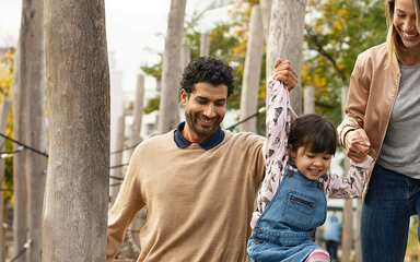 Eine Familie geht im Freien spazieren. Mutter, Vater und Tochter sind bei der AOK gut versichert.