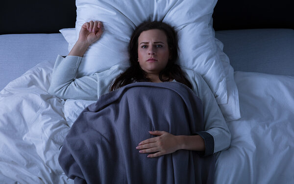 Eine Frau liegt mit geöffneten Augen im Bett – sie hat eine Schlafparalyse.