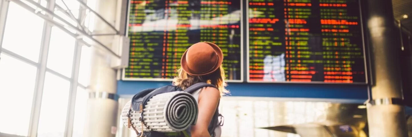 Junge Frau mit Rucksack guckt auf Anzeigentafel am Flughafen