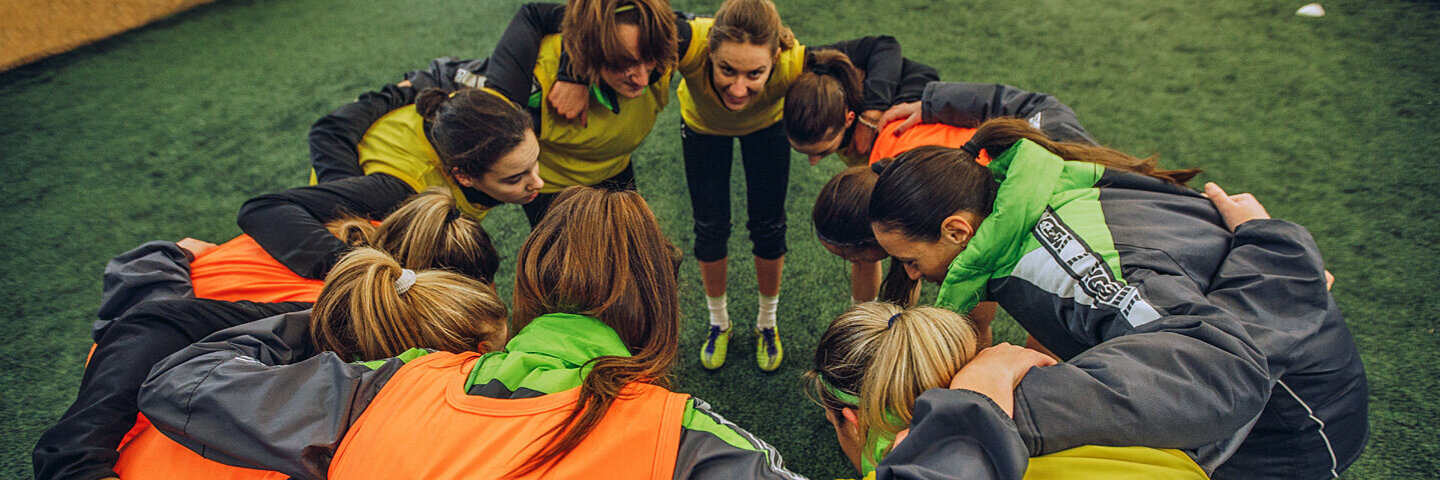 Frauen einer Fußballmannschaft stecken die Köpfe zusammen.