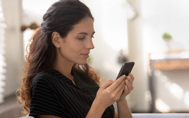 Eine junge Frau mit langen dunklen Haaren schaut nachdenklich auf ihr Smartphone.