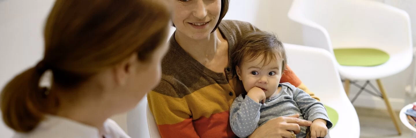 Mutter hält Baby auf dem Arm und bei schauen zu einer Kinderärztin.