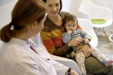 Mutter hält Baby auf dem Arm und bei schauen zu einer Kinderärztin.