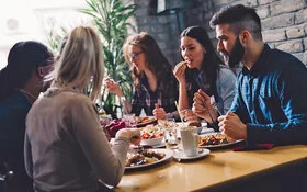 Ein Gruppe junger Menschen bei einem Geschäftsessen, eine von ihnen fürchtet, die anderen könnten ihre lauten Darmgeräusche hören.