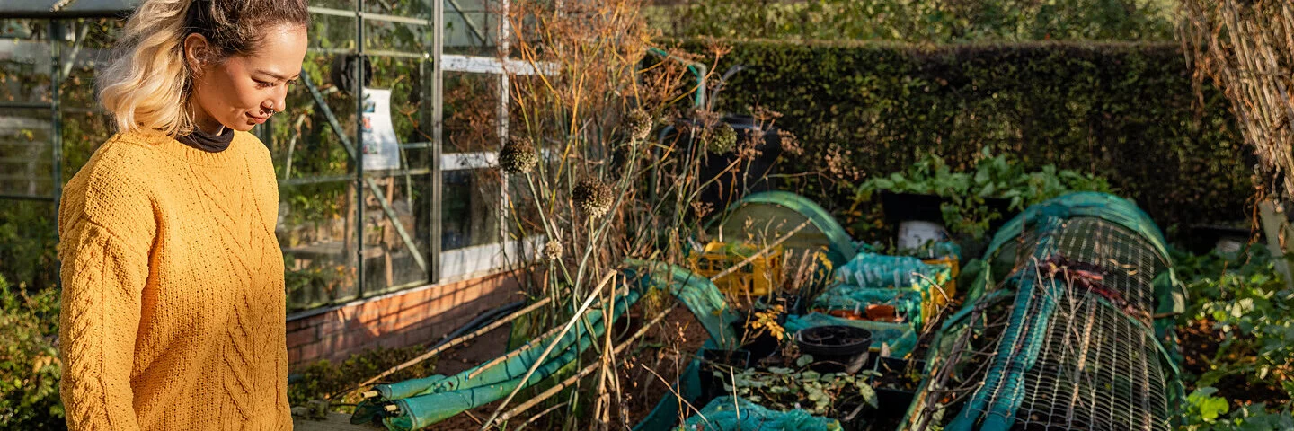 Frau geht durch ihren Schrebergarten, der nach dem Prinzip der Permakultur angelegt wurde.