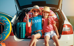 Kinder sitzen im Kofferraum mit Urlaubsgepäck und posieren