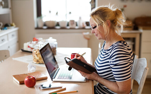 Eine Frau erarbeitet am Laptop und mit Planer einen Zeitplan für ein besseres Zeitmanagement.