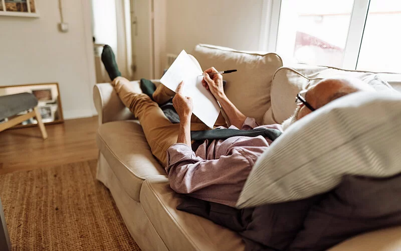 Ein älterer Mann liegt auf dem Sofa und macht sich einen Plan, um seine Ziele zu definieren.
