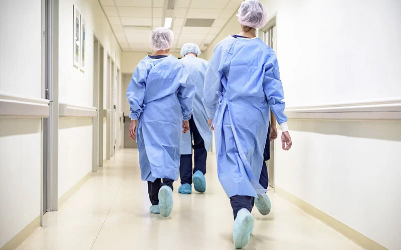 Pflegepersonal geht einen langen Gang in einem Krankenhaus entlang, ein laufintensiver Beruf mit starken Belastungen.