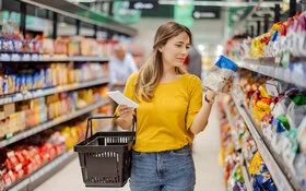 Eine junge Frau schaut sich beim Einkaufen im Supermarkt die Nährwertangaben eines Produktes an.